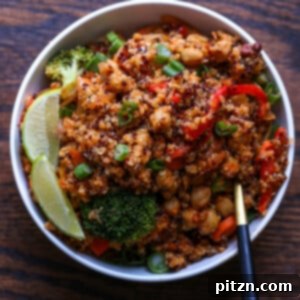 A hearty bowl of spicy quinoa chickpea casserole, garnished with a fresh lime wedge and green onions.