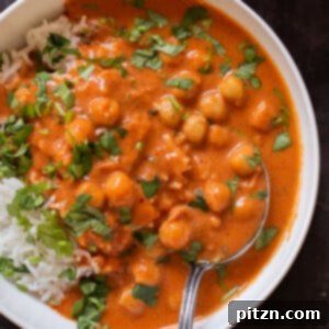 A close-up of a vibrant bowl of Indian butter chickpeas served over fluffy rice, garnished with fresh cilantro.