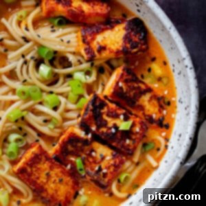 A steaming bowl of spicy peanut butter ramen, generously topped with crispy tofu, fresh green onions, and toasted sesame seeds.