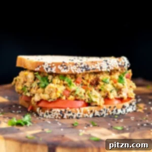 A wholesome Mediterranean chickpea salad sandwich resting on a rustic wooden board, garnished with fresh ingredients.