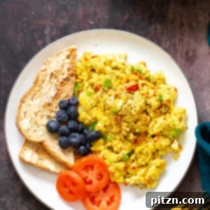 A fluffy vegan tofu scramble served with a side of golden-brown toast and vibrant sautéed vegetables for a complete breakfast.