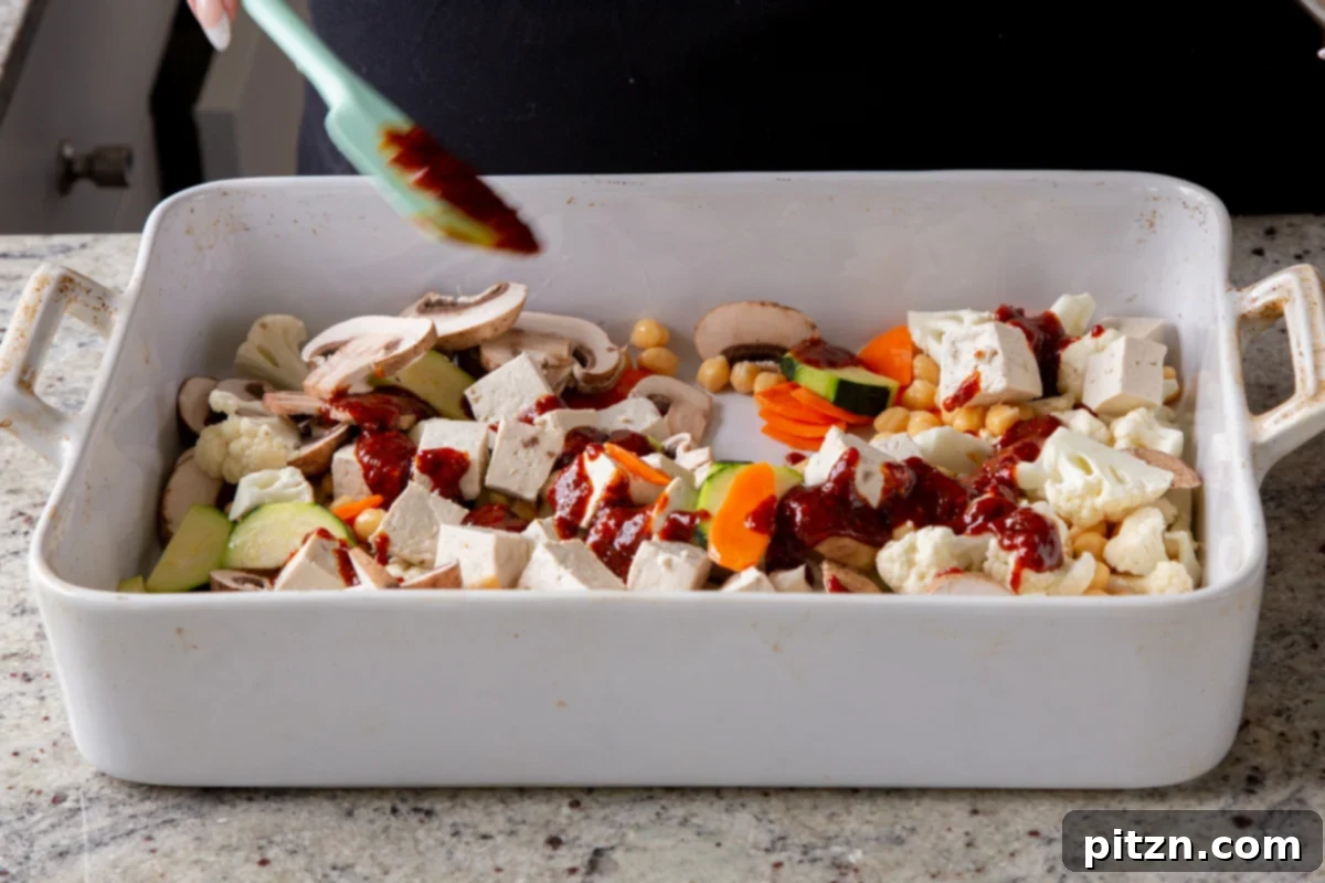 Pouring the red Gochujang marinade over the tofu and vegetables on the baking sheet.