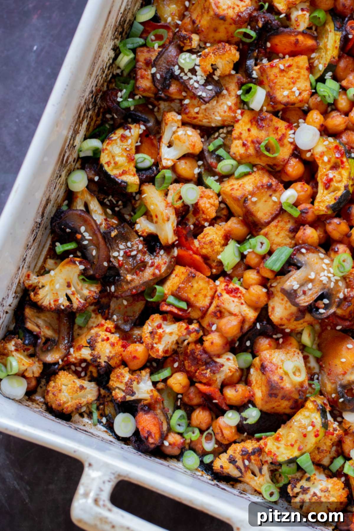 Close-up of golden-brown gochujang tofu and vegetables on a baking sheet, fresh from the oven.