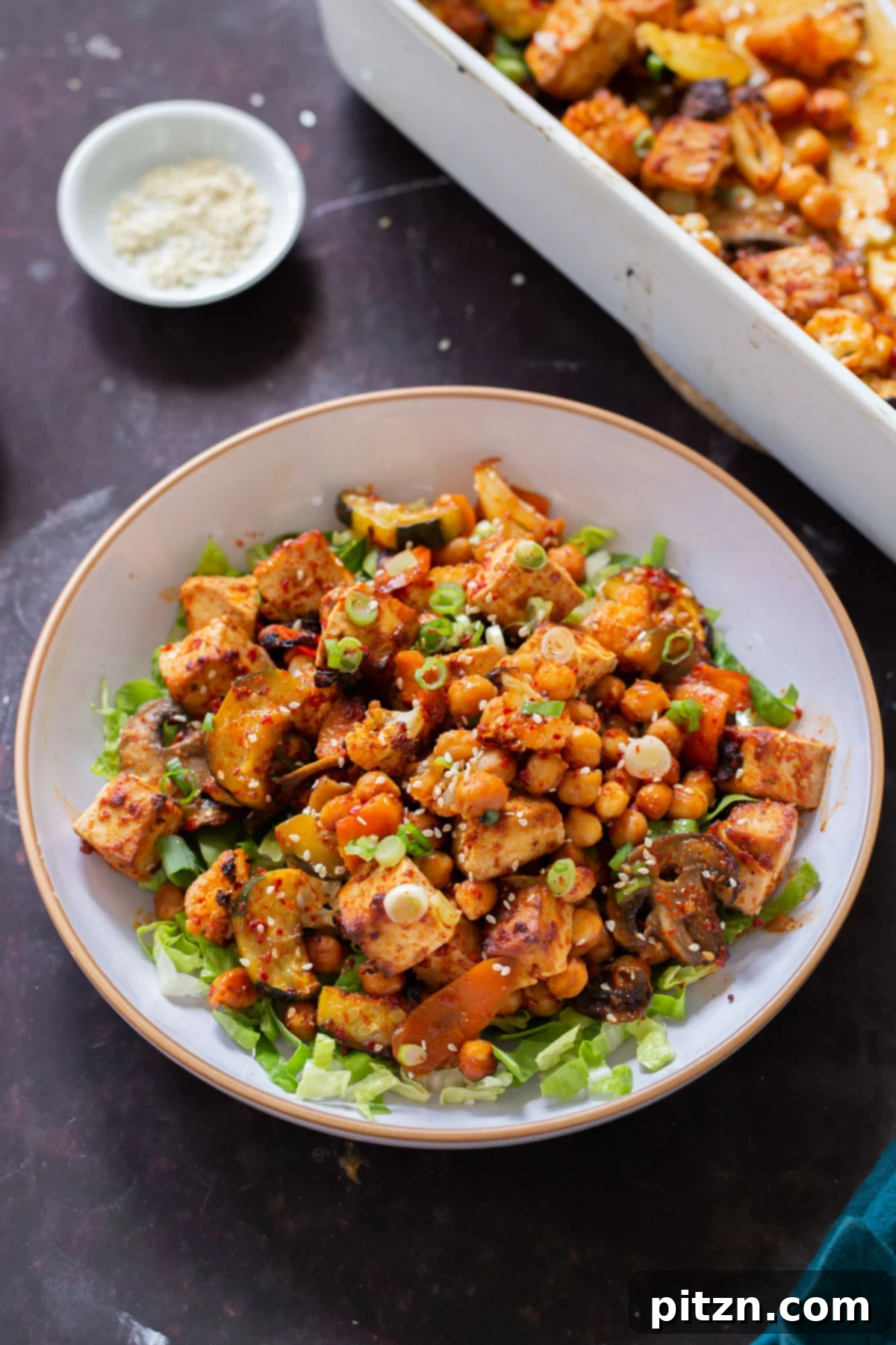 A vibrant gochujang tofu and veggie bowl next to the baking dish, showcasing the complete meal.