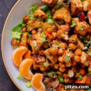Close-up of a colorful Gochujang tofu and veggie bowl, garnished with sesame seeds and orange segments.