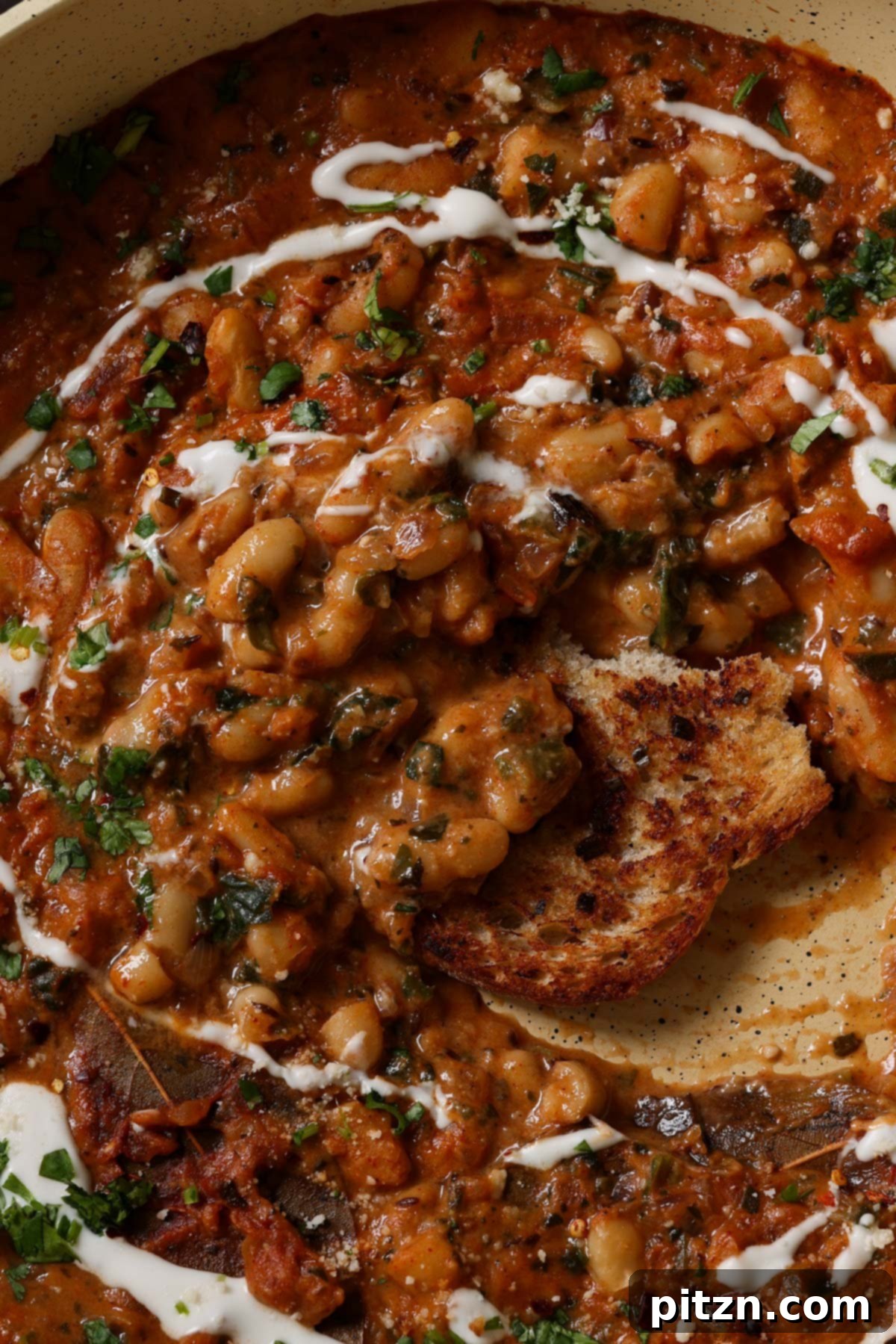 Close-up of dipping sourdough bread into a bowl of Dhaba White Bean Curry, garnished with fresh cilantro.