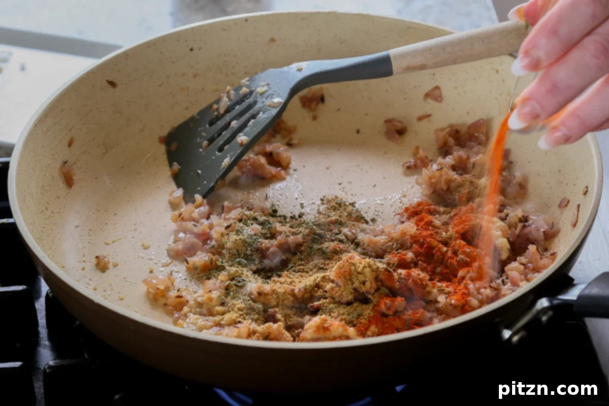 Various dried ground spices being sprinkled into the pan with the cooked onions.