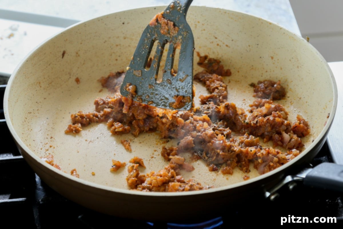 The ground spices being thoroughly mixed into the caramelized onions in the pan, creating a fragrant paste.