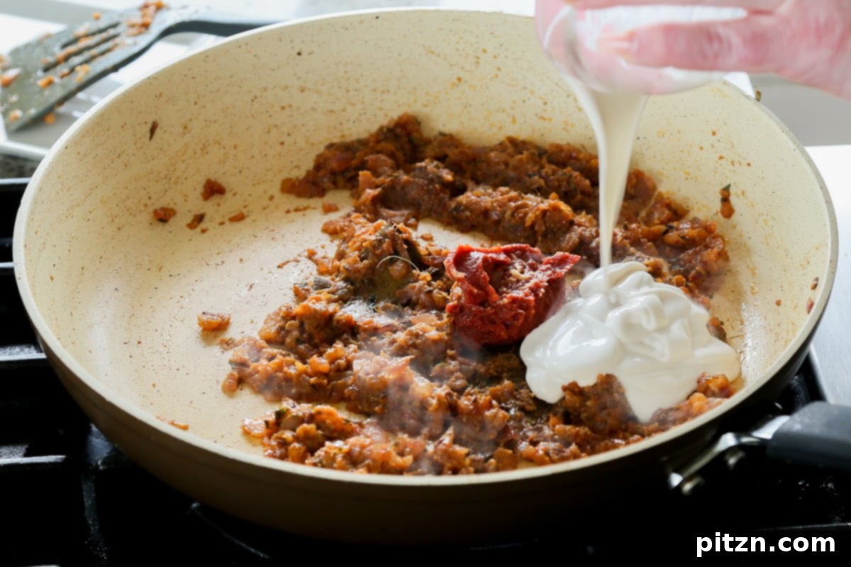 Tomato paste and non-dairy yogurt being added to the spiced onion mixture in the pan.