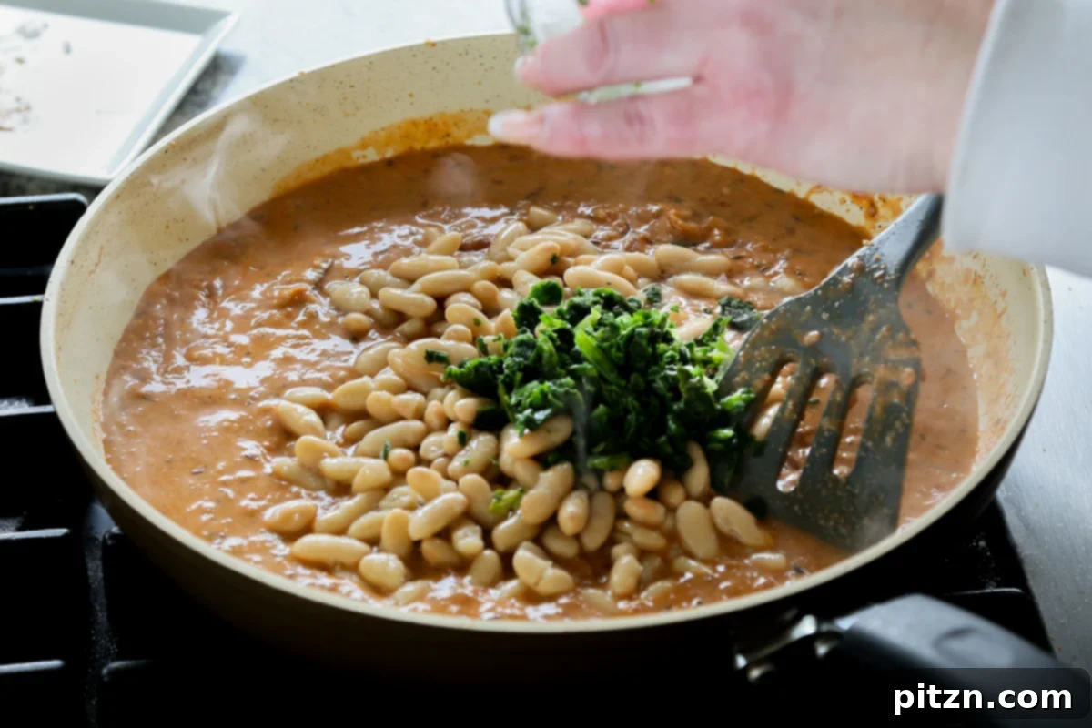Drained white beans and thawed spinach being added to the simmering curry sauce.