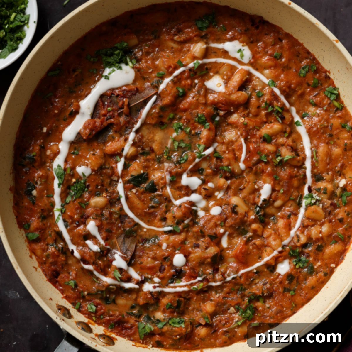 A completed pan of Dhaba White Bean Curry, beautifully garnished with red pepper flakes, fresh cilantro, and a swirl of non-dairy yogurt, ready to be enjoyed.
