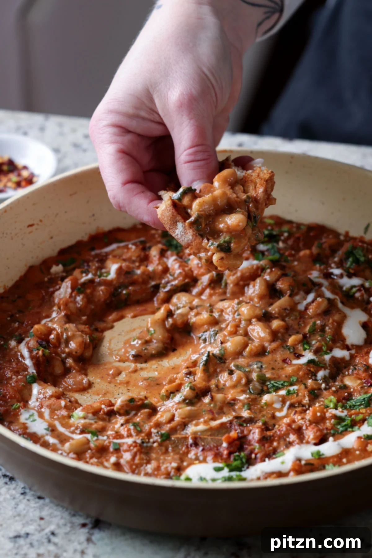 Sourdough bread being dipped into a rich Dhaba White Bean Curry, highlighting the creamy texture of the sauce.