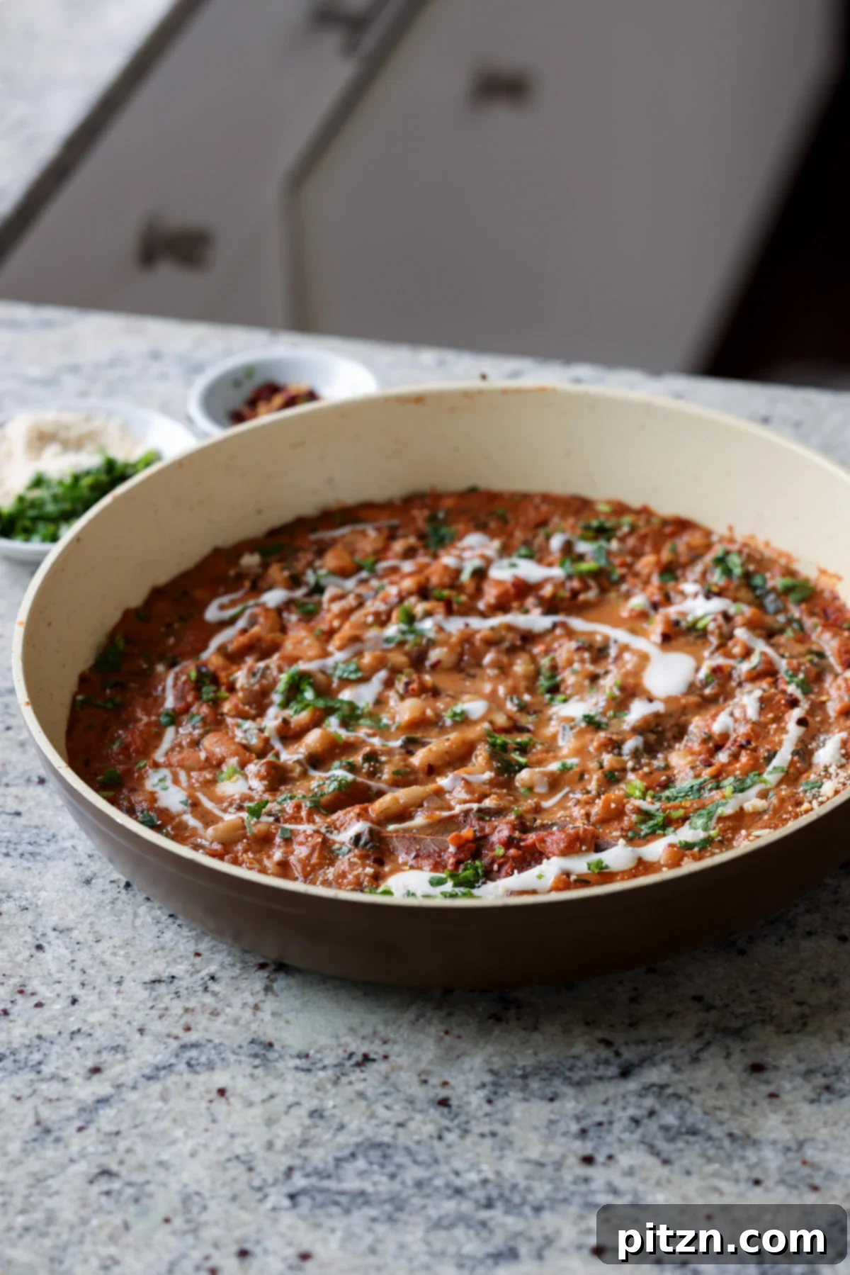 A pan of Dhaba White Bean Curry, garnished with red pepper flakes, fresh cilantro, and a swirl of non-dairy yogurt, ready to serve.