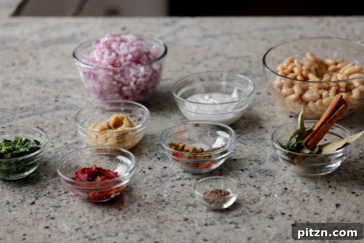 Bowls of various Dhaba White Bean Curry ingredients including spices, tomato paste, and non-dairy yogurt laid out on a kitchen counter, ready for cooking.