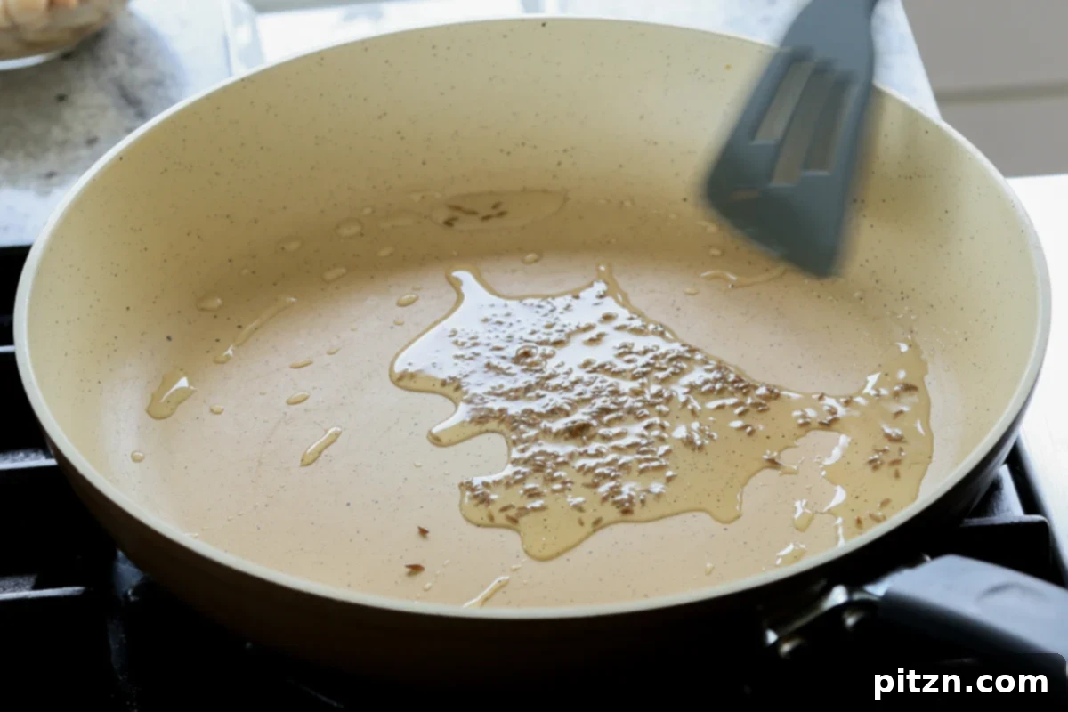 Close-up image of cumin seeds toasting in a hot pan with oil, releasing their fragrance.