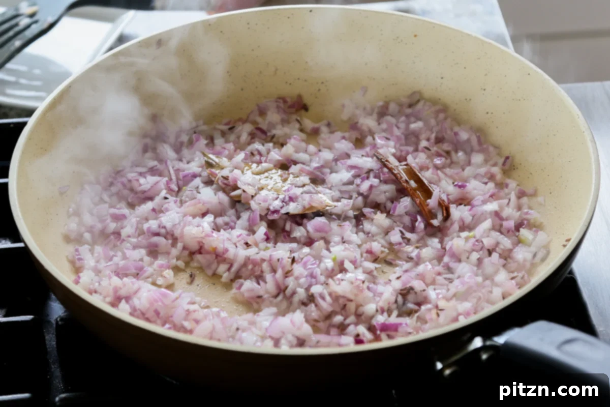 Freshly chopped red onions being added to a pan with toasted whole spices and oil.