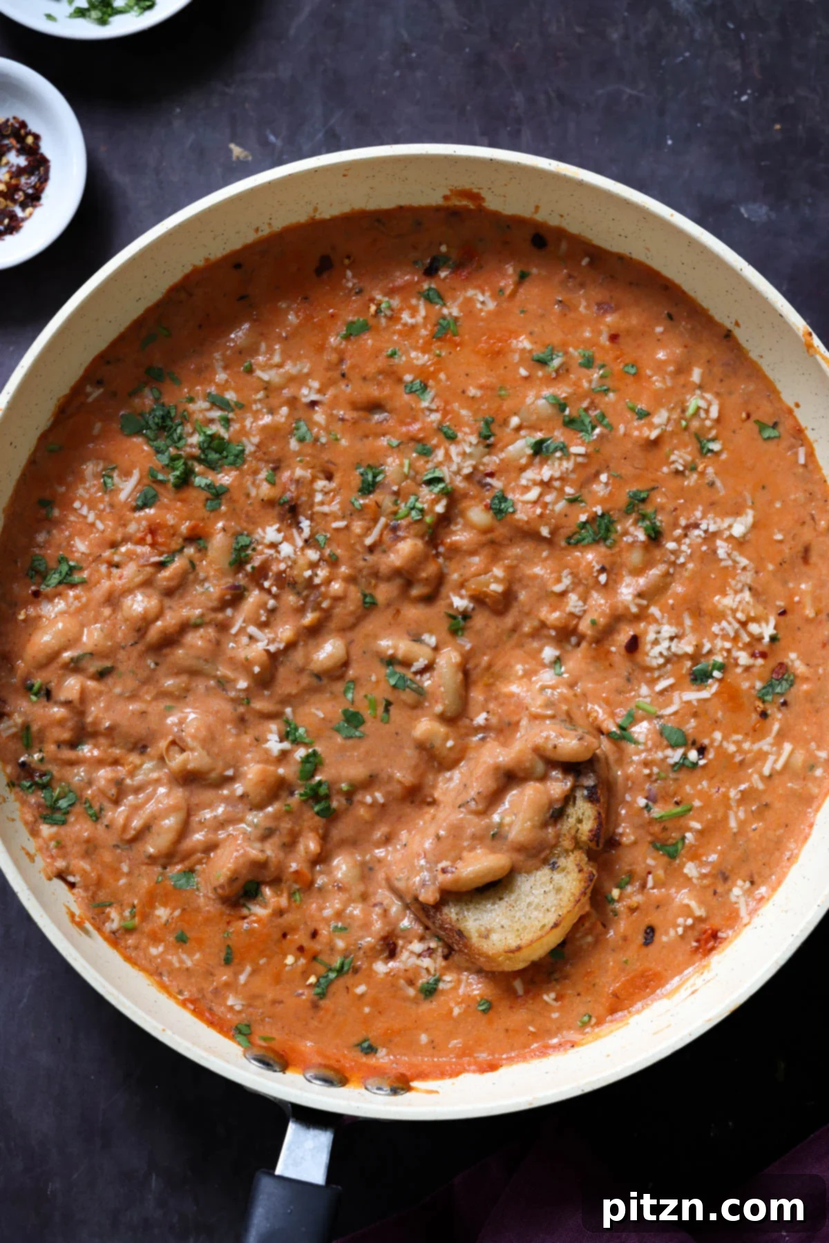 Effortless Rosé Beans for All 2 Delicious rosé sauce beans in a pan with sourdough bread being dipped into the creamy sauce, ready to be enjoyed.