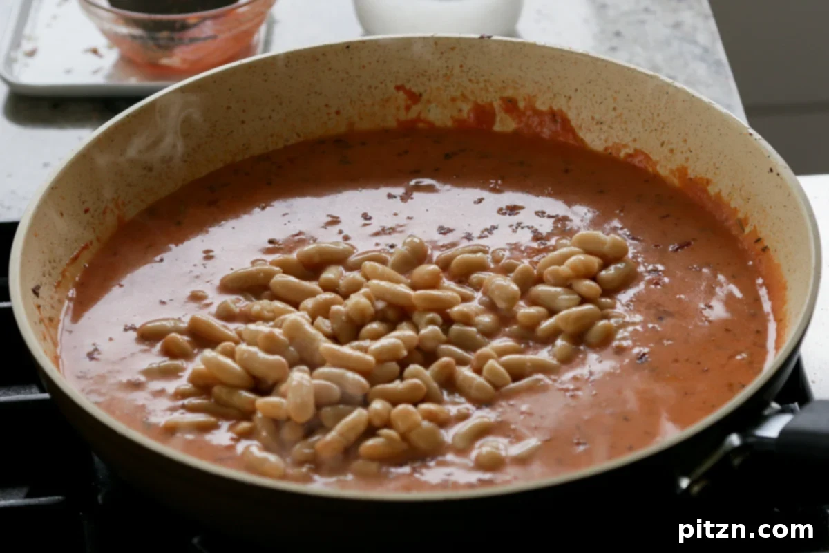 Effortless Rosé Beans for All 11 Adding white beans to the rosé sauce in the pan for simmering.
