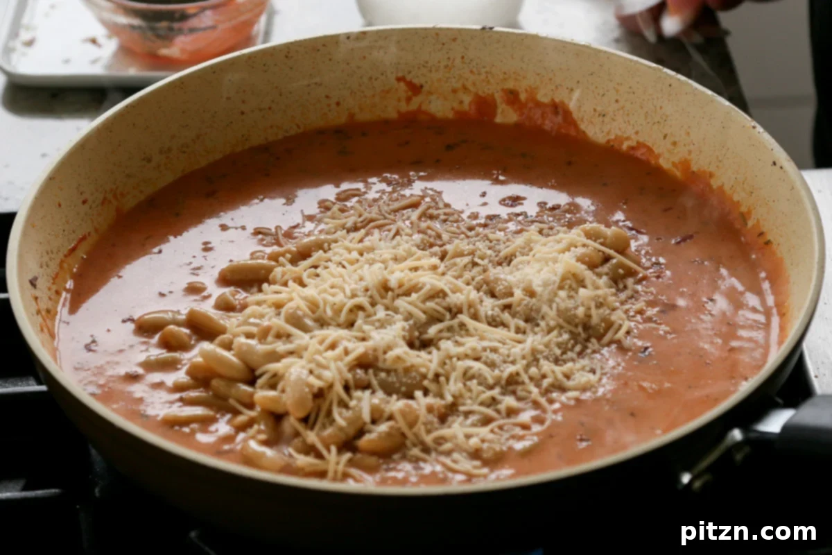 Effortless Rosé Beans for All 12 Sprinkling vegan Parmesan cheese over the rosé sauce beans in the pan.