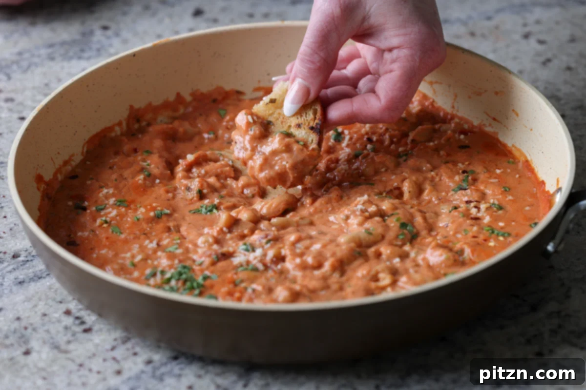 Effortless Rosé Beans for All 14 Someone dipping sourdough bread into the creamy rosé sauce with white beans directly from the pan, showcasing its deliciousness.
