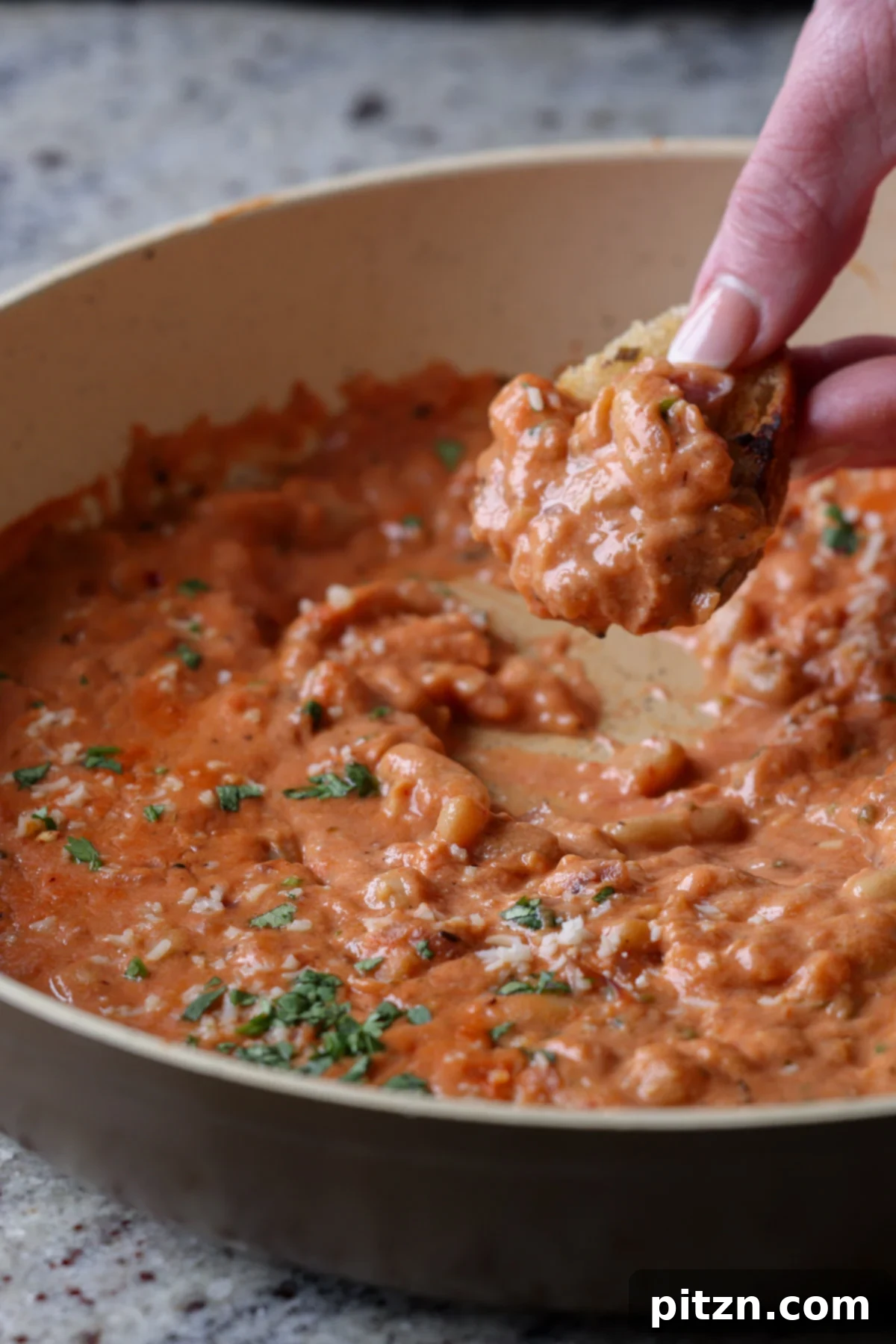 Effortless Rosé Beans for All 3 Close-up of a piece of sourdough bread being dipped into the creamy vegan rosé sauce with white beans in a skillet.
