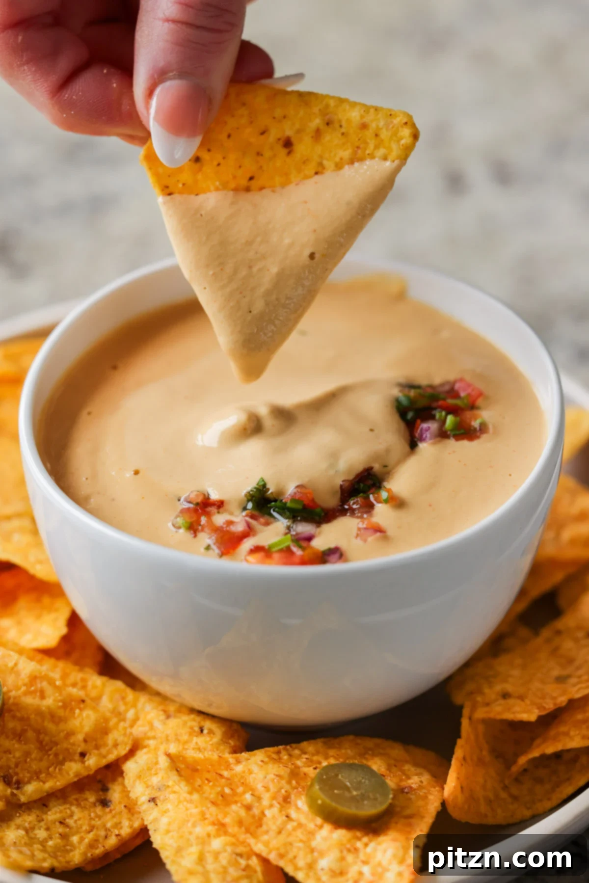 Amazing Cashew Nacho Cheese Gluten Free Oil Free Soy Free Choice 4 A hand dipping a crispy, golden tortilla chip into a generous bowl of creamy cashew nacho cheese sauce