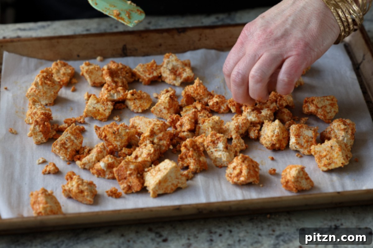 Tofu Kondattam: Crispy & Spicy South Indian Tofu 12 Spreading seasoned tofu pieces onto a parchment-lined baking sheet in a single layer