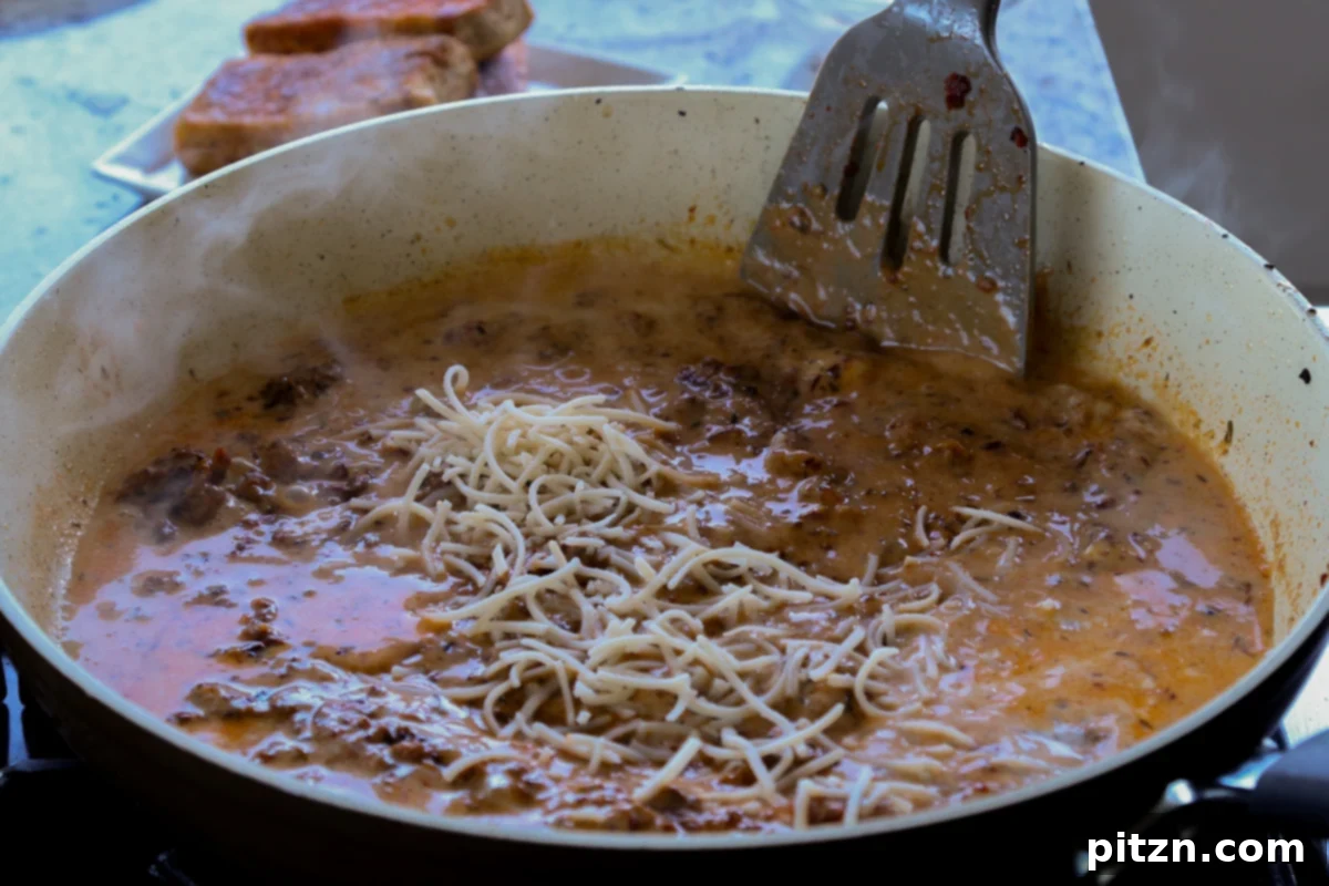 Vegan Marry Me Chicken Pasta 19 Adding vegan Parmesan cheese to the creamy pasta sauce in the skillet