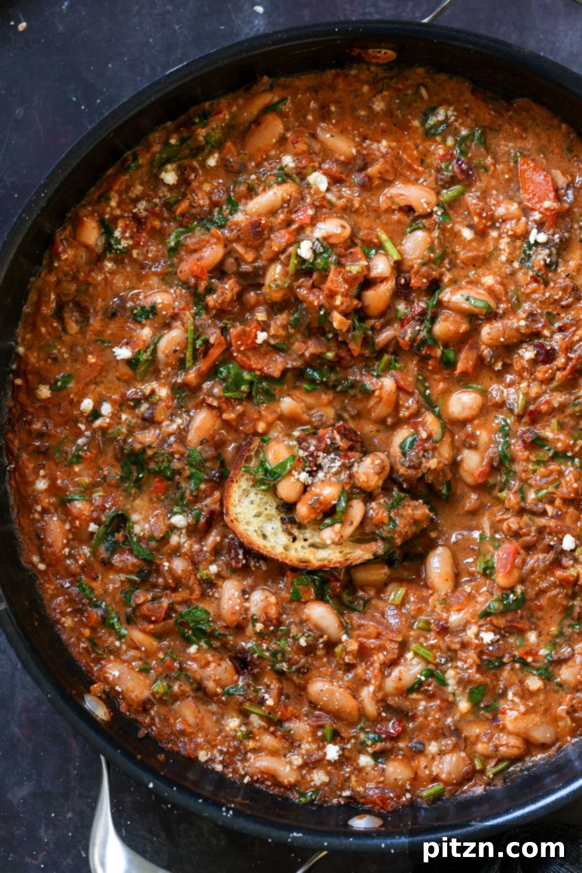 Weeknight Skillet Sausage and White Bean Pasta 2 Toasted sourdough bread being dipped into a luscious vegan sausage pasta sauce with white beans in a skillet, showcasing the dish's rich texture and inviting aroma.