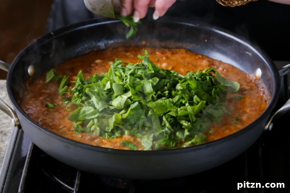 Weeknight Skillet Sausage and White Bean Pasta 20 Fresh chopped spinach being added to the hot vegan sausage pasta sauce, ready to wilt and add vibrant color and nutrients.