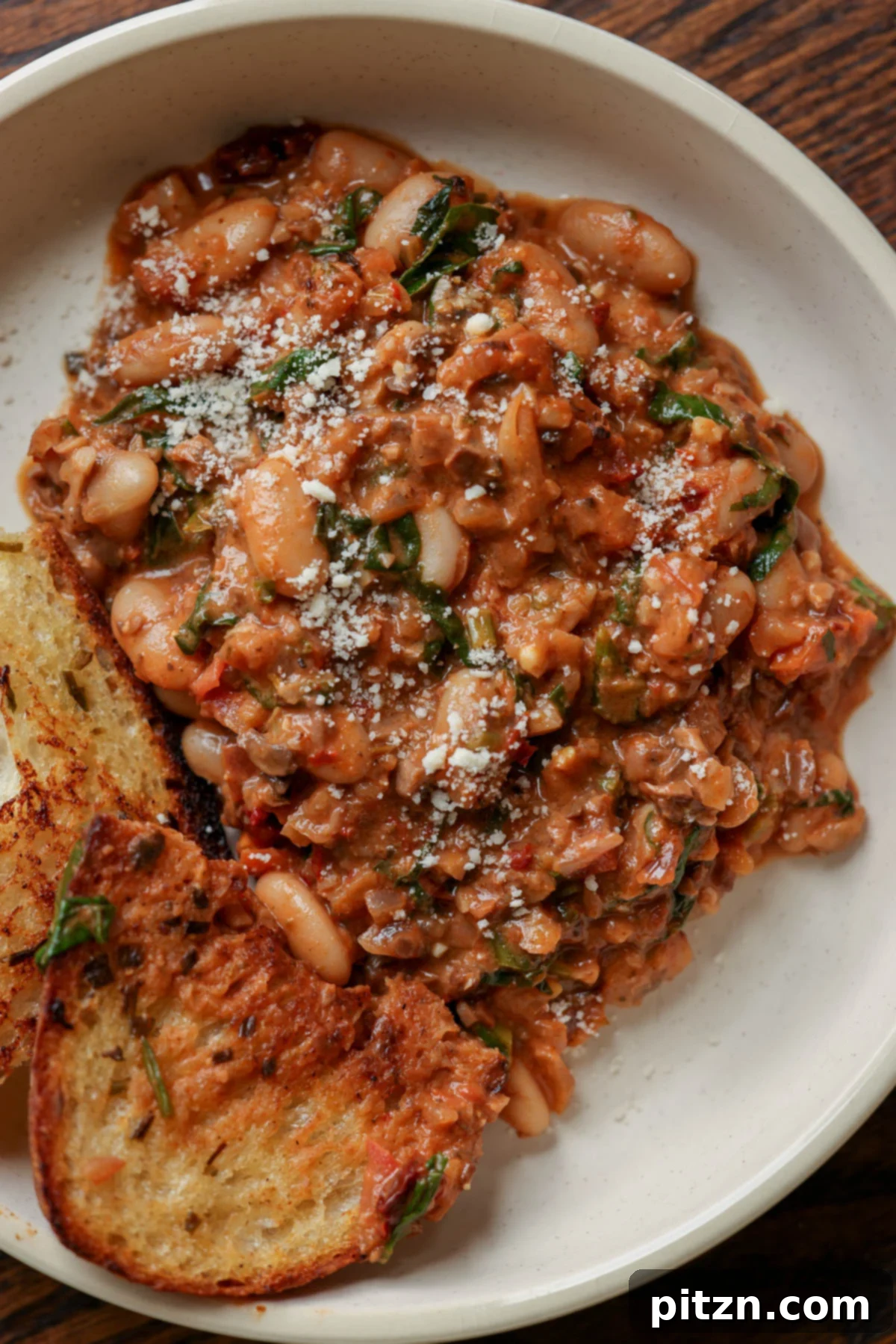 Weeknight Skillet Sausage and White Bean Pasta 4 A delicious serving of vegan sausage pasta sauce with white beans on a white plate, accompanied by a piece of toasted sourdough bread on the side, ready to be enjoyed.