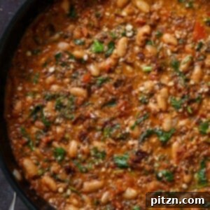 A vibrant close-up of vegan sausage pasta sauce simmering in a pan, garnished with fresh herbs, ready to be served.