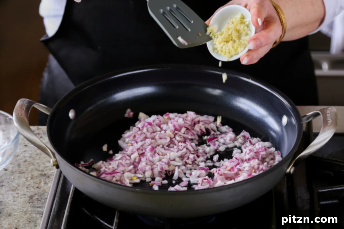 Weeknight Skillet Sausage and White Bean Pasta 7 Adding finely chopped red onion and minced garlic to the hot oil in the skillet, ready to be sautéed until translucent.