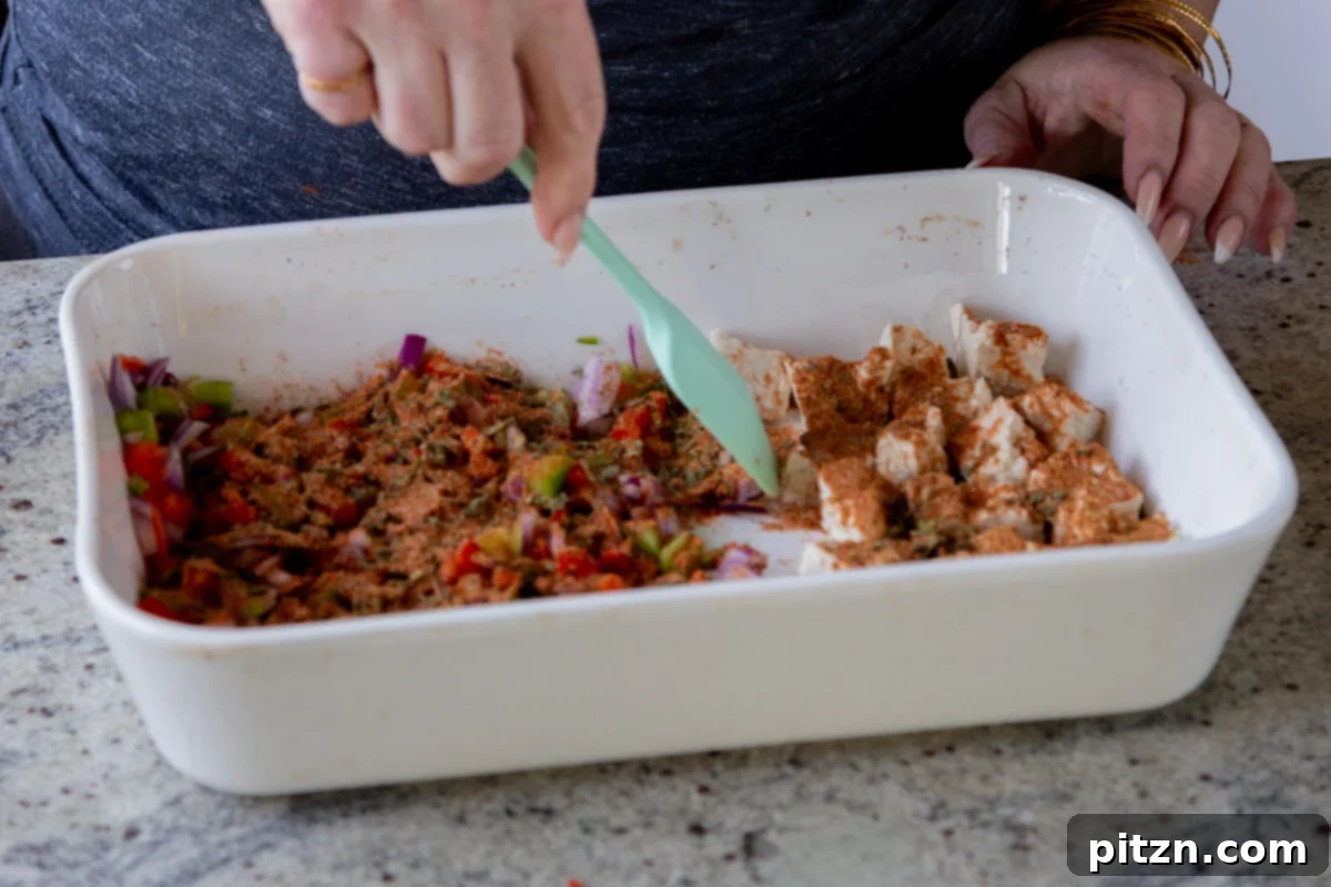 Fragrant Tikka Masala Rice Bake with Golden Crispy Tofu 13 A hand gently tossing spices with torn tofu pieces in a baking pan, ensuring even coating before baking.
