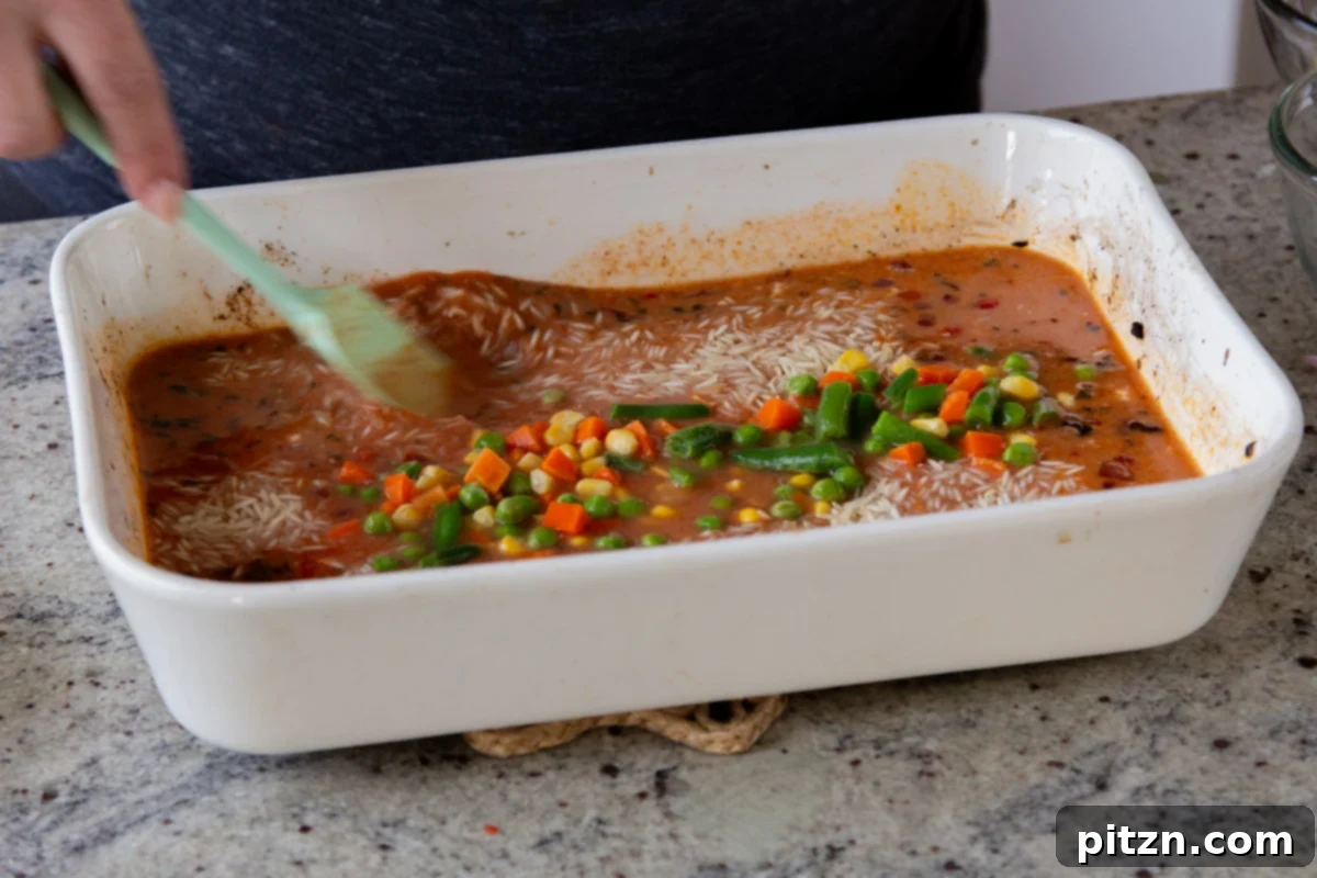 Fragrant Tikka Masala Rice Bake with Golden Crispy Tofu 17 Frozen mixed vegetables being added to the baking pan with rice and sauce, ready for the final bake.