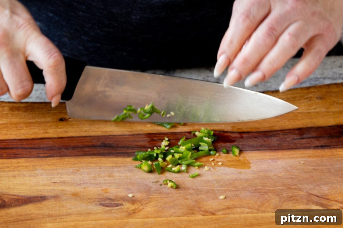 Fragrant Tikka Masala Rice Bake with Golden Crispy Tofu 7 A hand finely chopping a vibrant green chili on a cutting board, preparing it for the Tikka Masala Rice Bake.