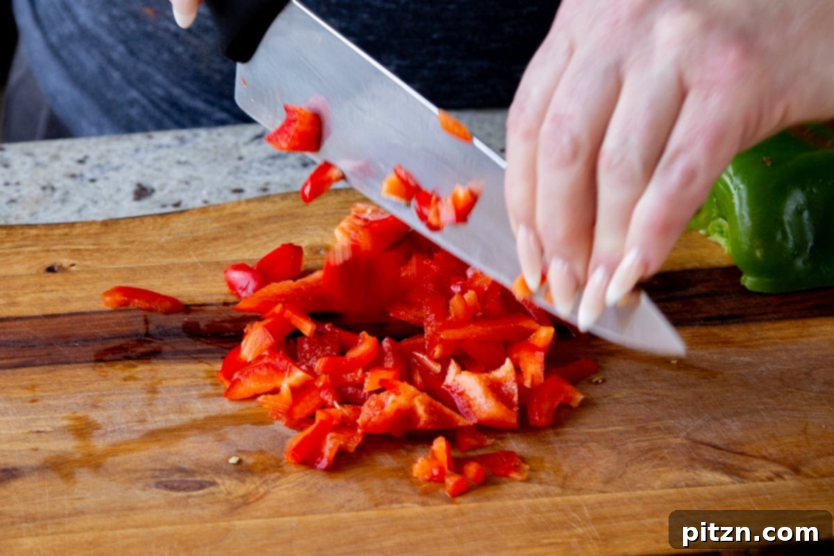 Fragrant Tikka Masala Rice Bake with Golden Crispy Tofu 8 A hand expertly chopping a red bell pepper into uniform pieces on a wooden cutting board, adding color to the dish.