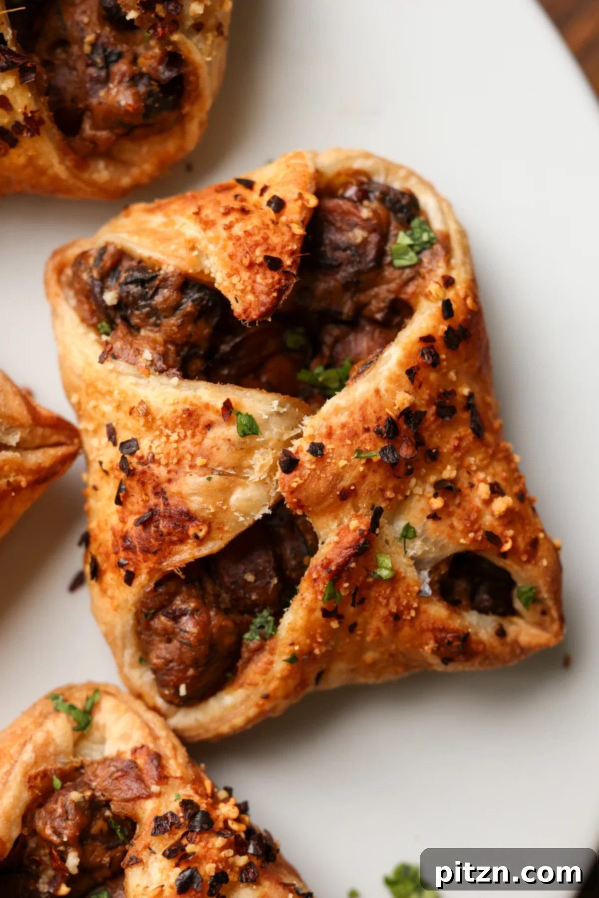 Close-up of golden brown creamy mushroom puffs on a white serving plate, garnished with fresh herbs.
