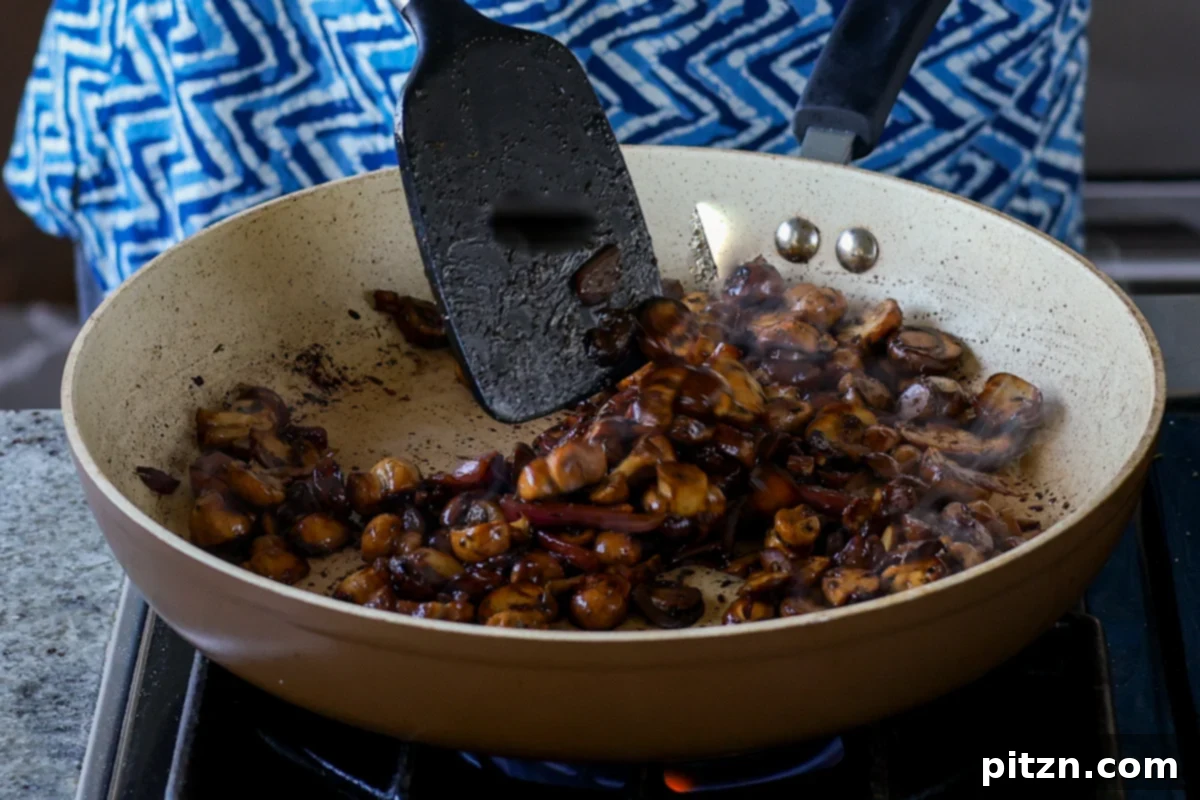 Stirring the mushroom mixture with added spices and balsamic vinegar, ensuring even cooking and flavor distribution.