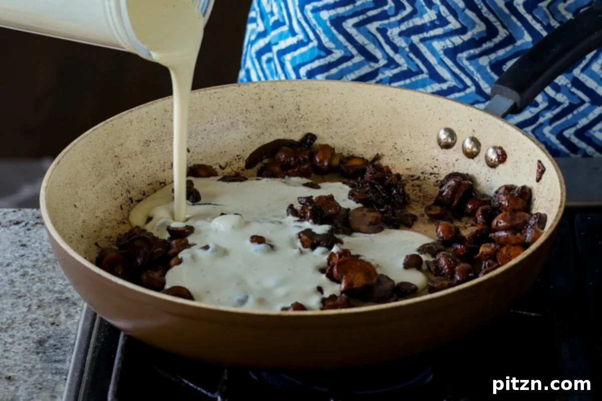 Pouring the freshly blended cream sauce directly into the pan with cooked mushrooms, preparing for the final filling.