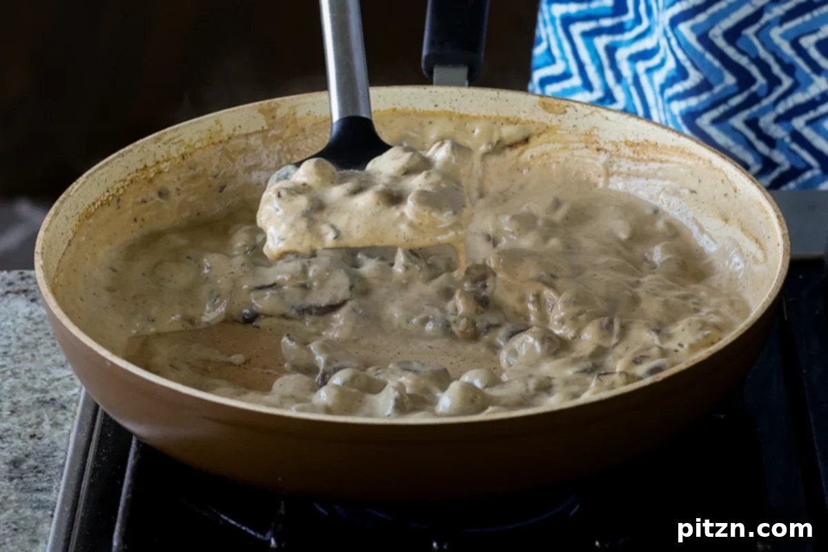 Close-up of the thickened cream sauce clinging to a spatula, indicating the perfect consistency for the mushroom puff filling.