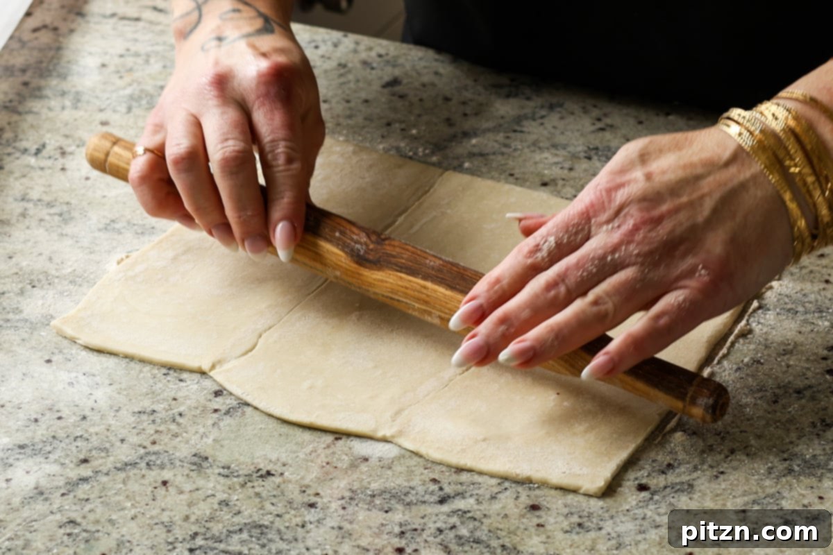 Rolling out puff pastry dough on a lightly floured surface with a rolling pin to achieve a larger, thinner sheet.