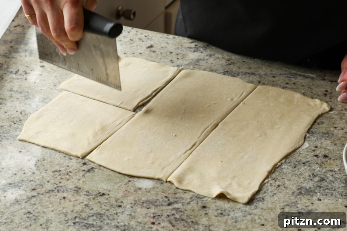 Cutting the rolled-out puff pastry sheet into equal rectangles, preparing for filling and folding.