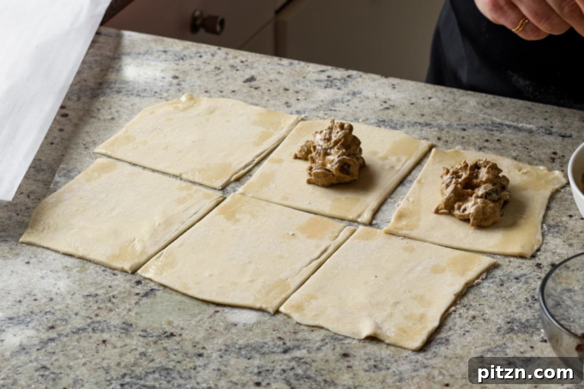 Scooping creamy mushroom filling onto the center of a puff pastry square, leaving edges clear for sealing.