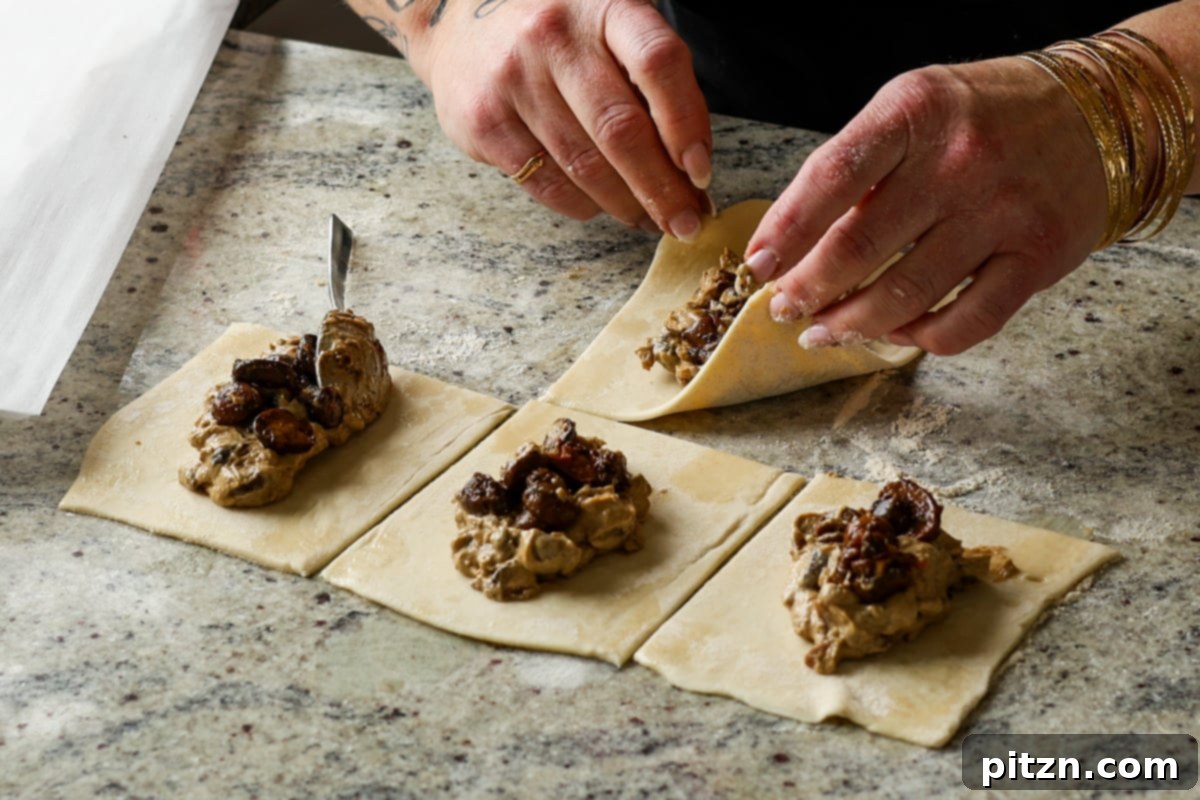 Carefully folding the corners of the puff pastry over the filling and pressing to seal, creating the mushroom puff shape.