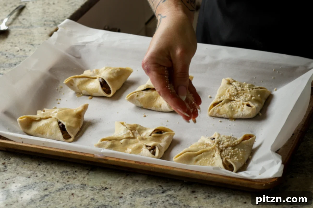 Sprinkling sesame seeds and pepper flakes over the brushed mushroom puffs on a baking sheet, ready for baking.