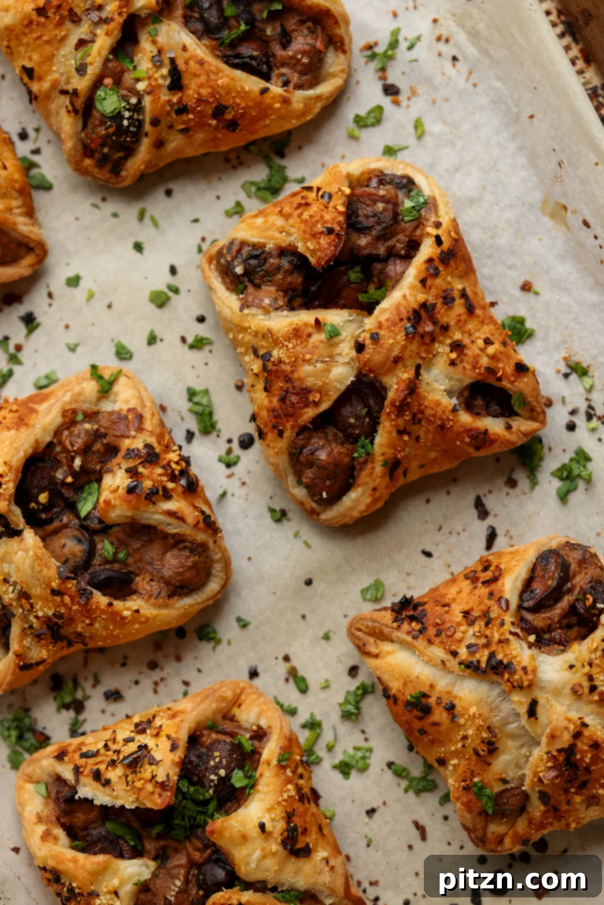 Baked mushroom puffs arranged neatly on a parchment-lined baking sheet, glistening and golden.
