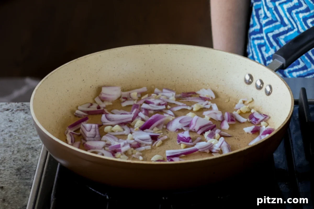 Sautéing chopped onions and minced garlic in a pan, the first step for building flavor in the mushroom filling.