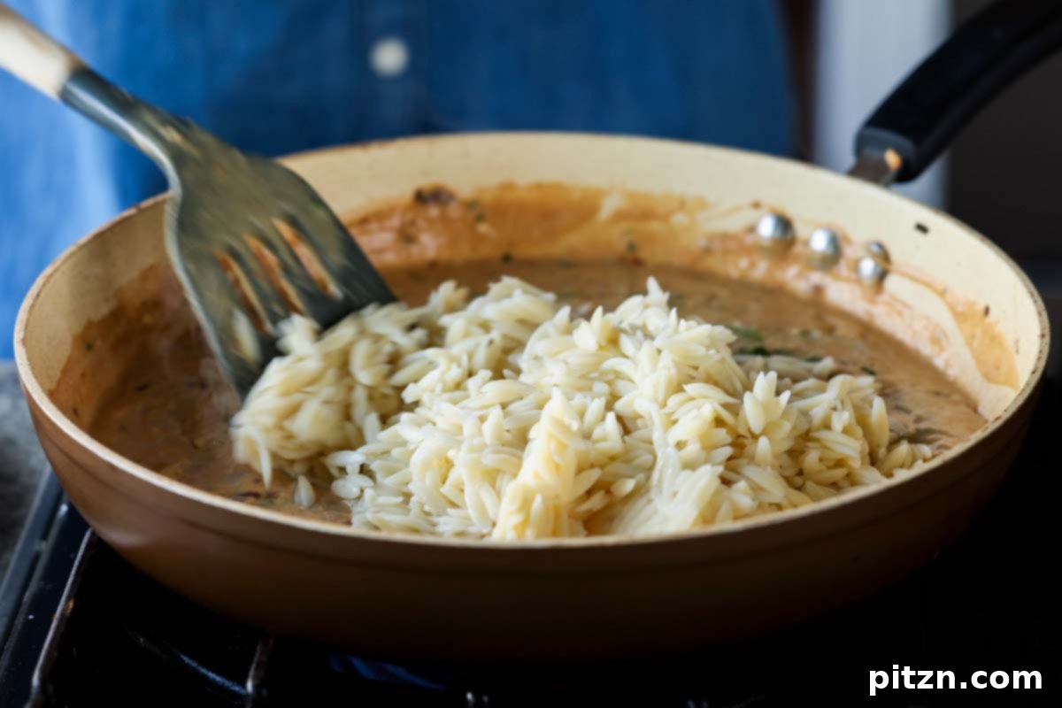 Golden Paprika Tofu with Creamy Garlic Parmesan Orzo 24 Adding cooked orzo pasta to the creamy garlic parmesan sauce in the pan.