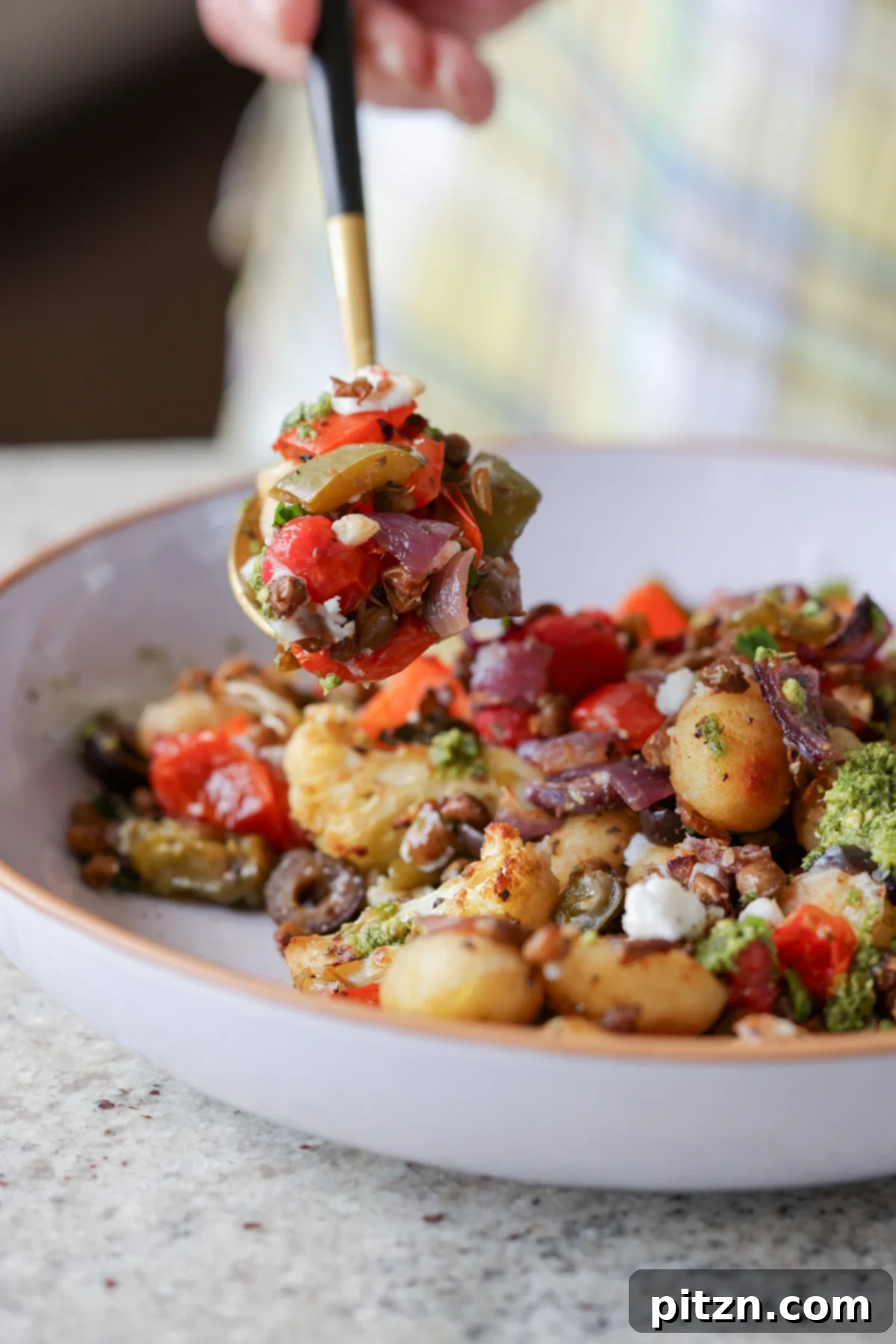 One-Pan Mediterranean Gnocchi: No Boil, Big Flavor 5 A close-up of a spoon scooping a bite of sheet pan gnocchi, vegetables, and vegan feta.